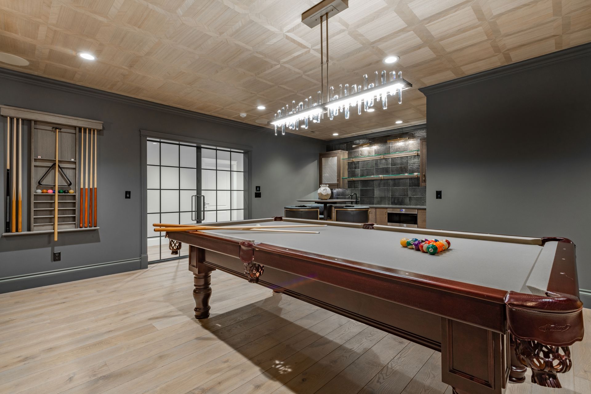 Pool table in a modern, dark-painted game room with bar and decorative ceiling lighting.