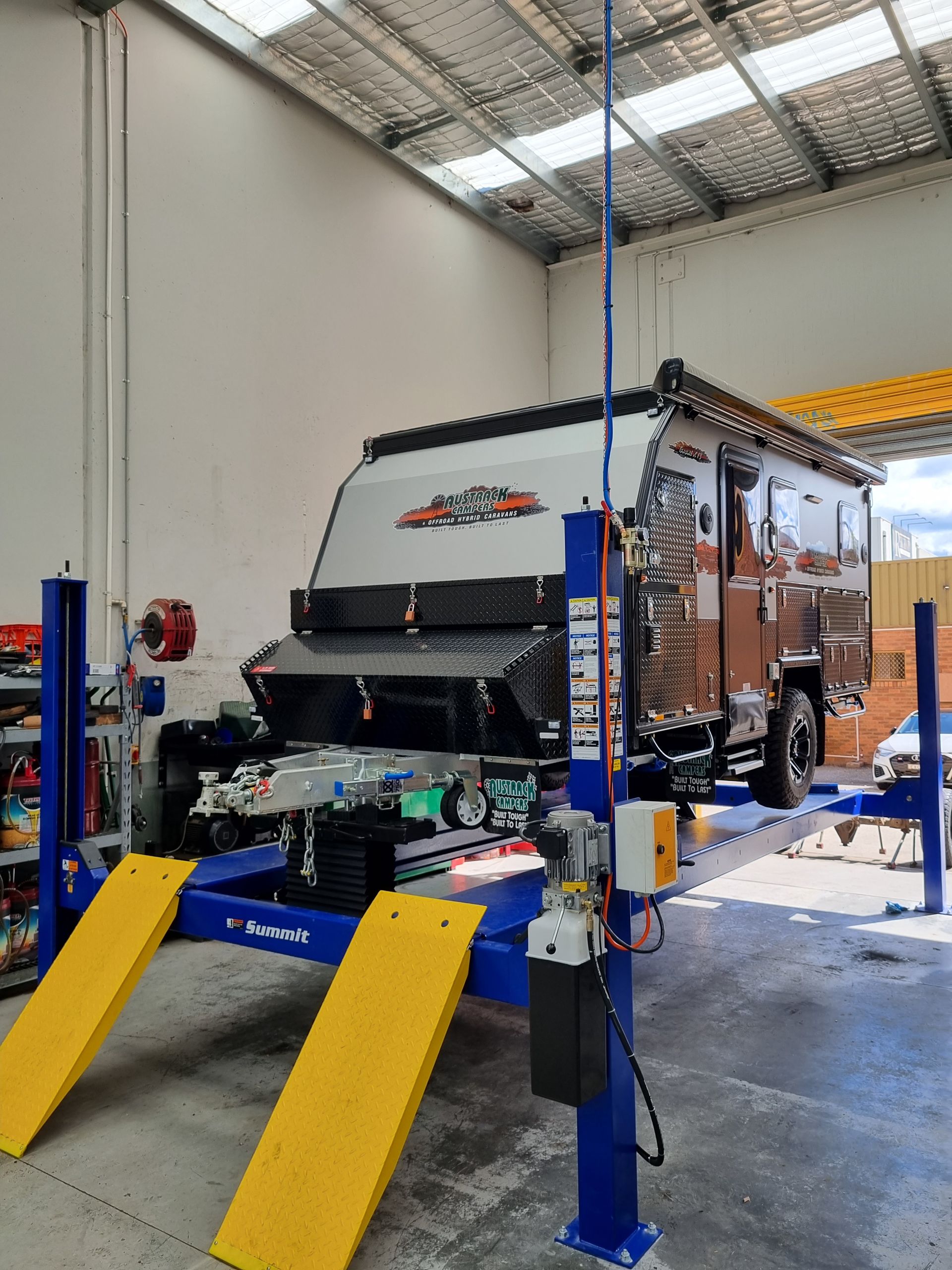 Caravan on a blue car lift inside a garage. The caravan is brown and black, with a retractable awning — Cartech Australia in Albury, NSW