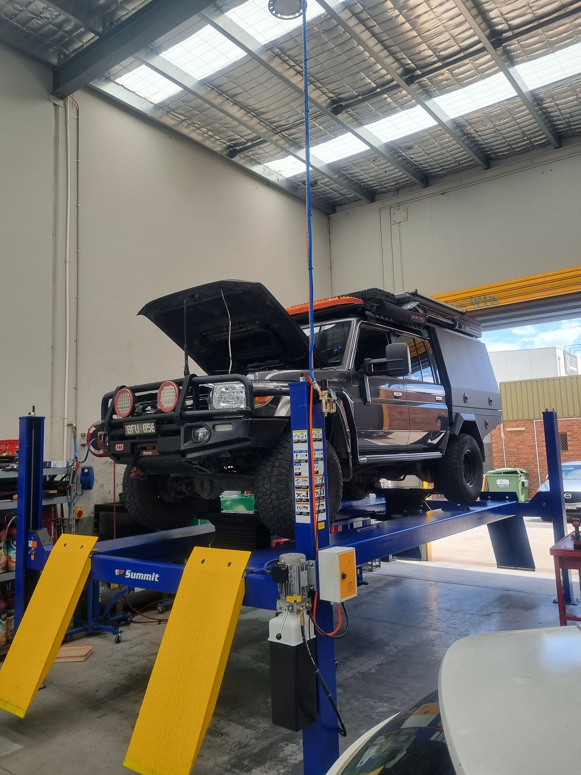 Dark SUV on a blue and yellow car lift in a workshop, hood open — Cartech Australia in Albury, NSW