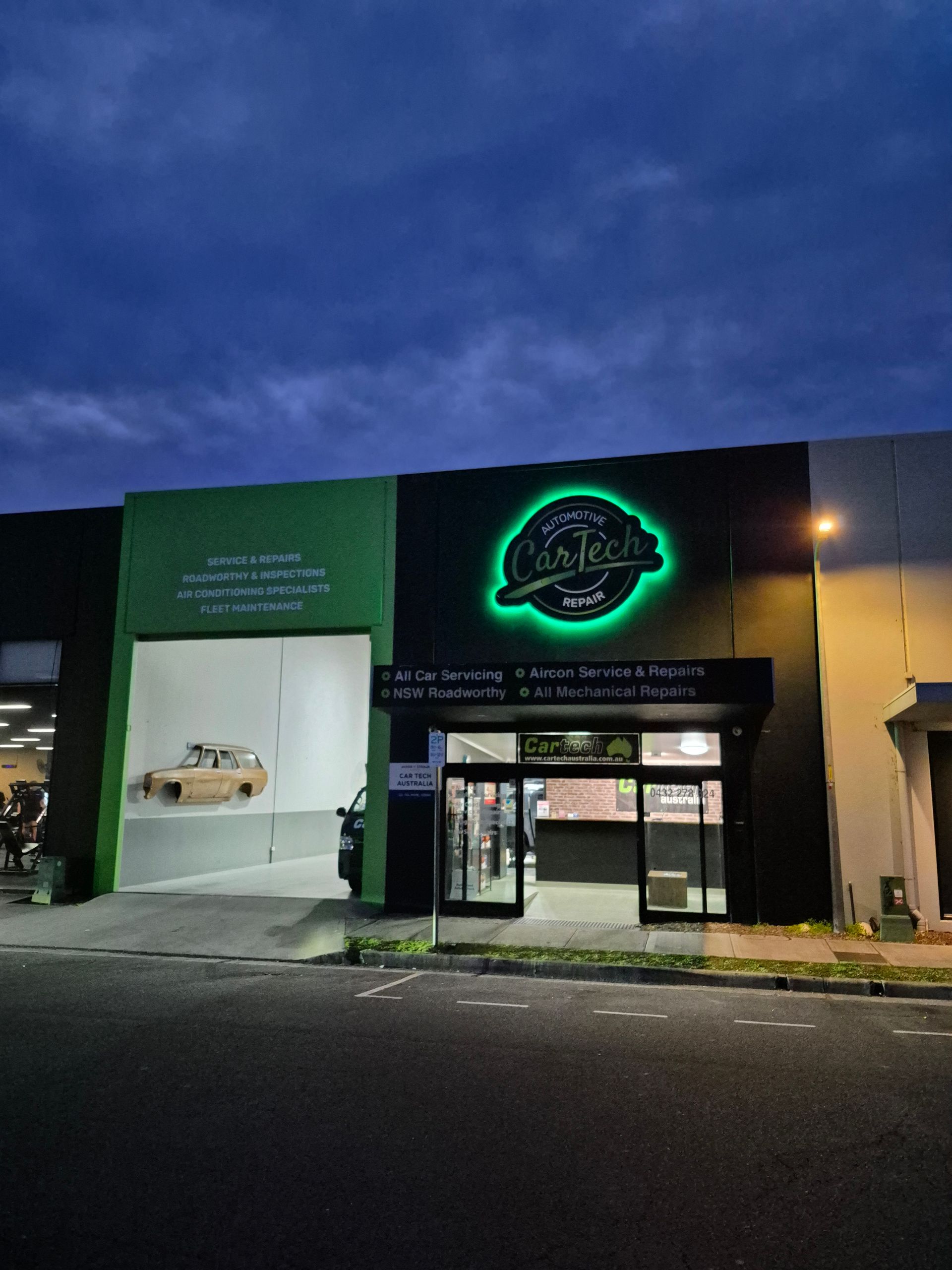 Green and black building with illuminated sign, car visible inside. Dusk setting — Cartech Australia in Albury, NSW