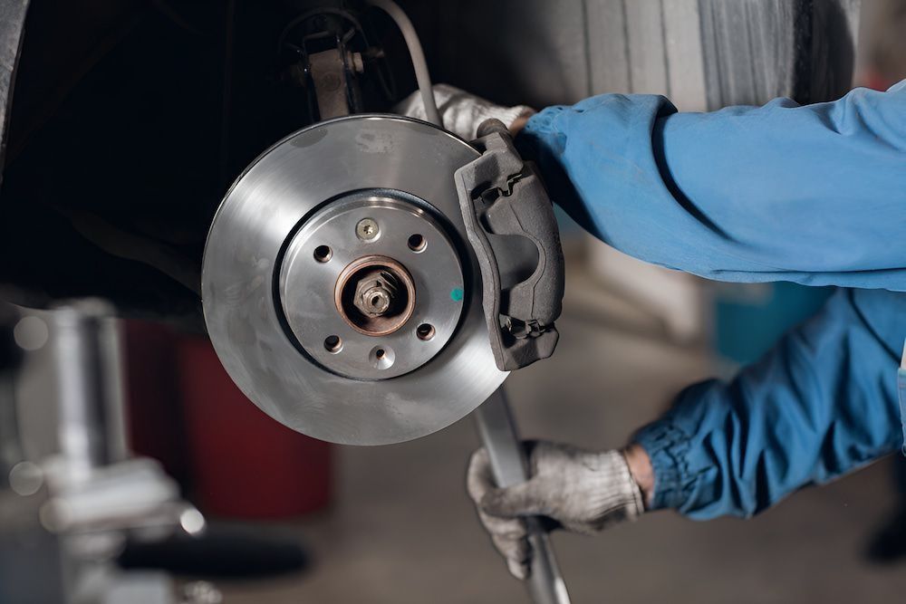 Mechanic inspecting and replacing car brake disc and caliper during vehicle service in workshop