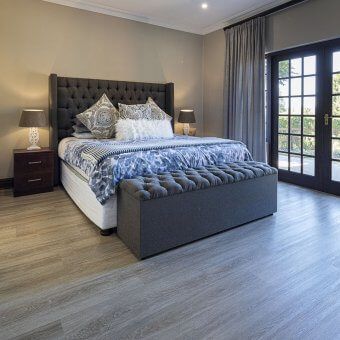 A bedroom with a king size bed , ottoman , nightstand , and sliding glass doors.