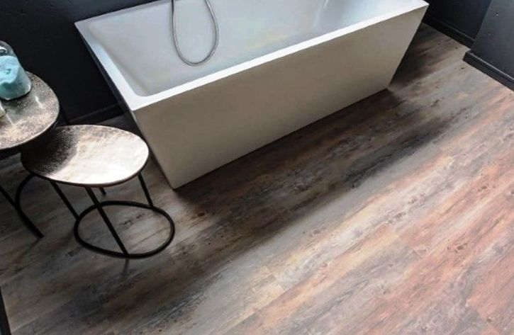 A bathtub is sitting on a wooden floor in a bathroom next to two tables.