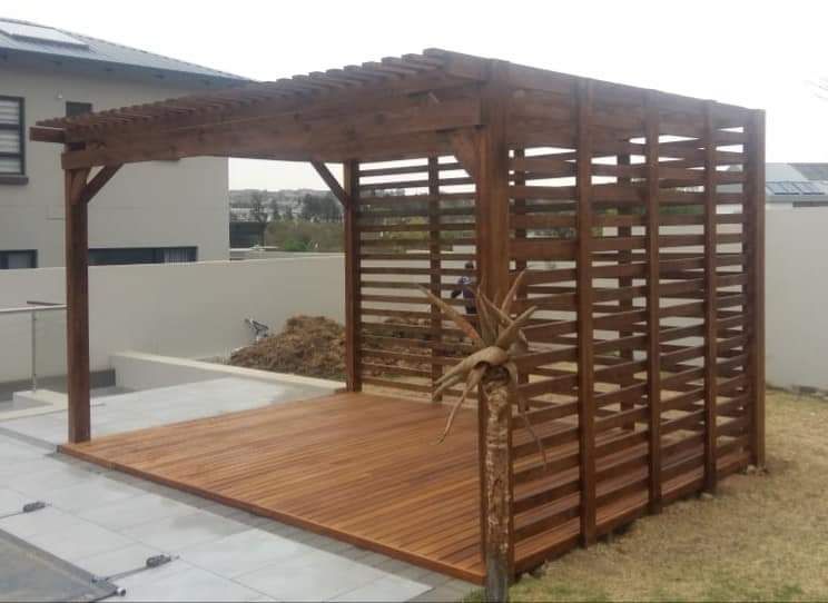 A wooden pergola with a wooden deck in front of a house.