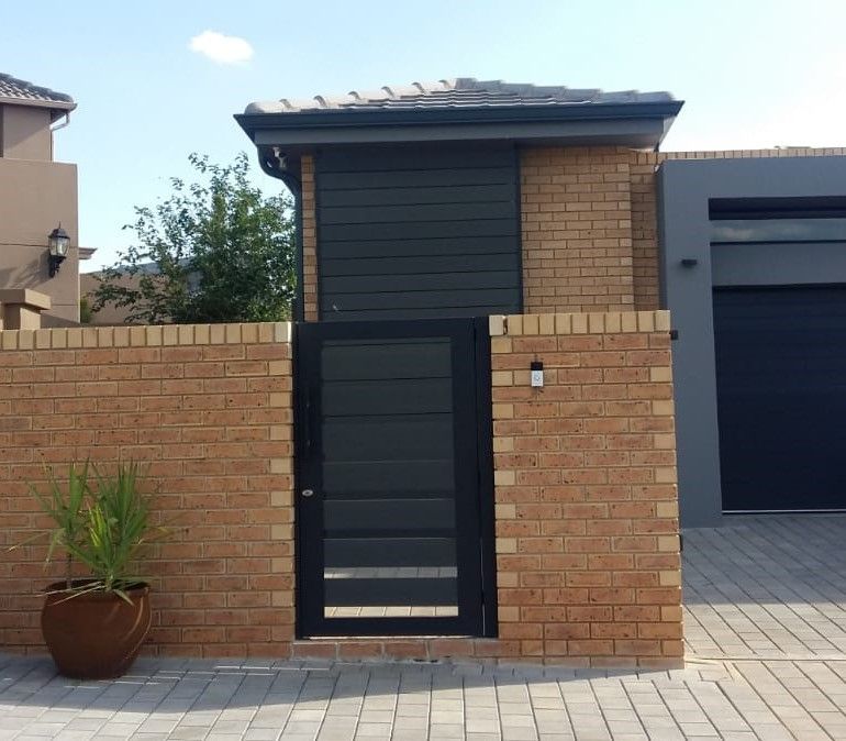A brick wall with a black gate in front of a house