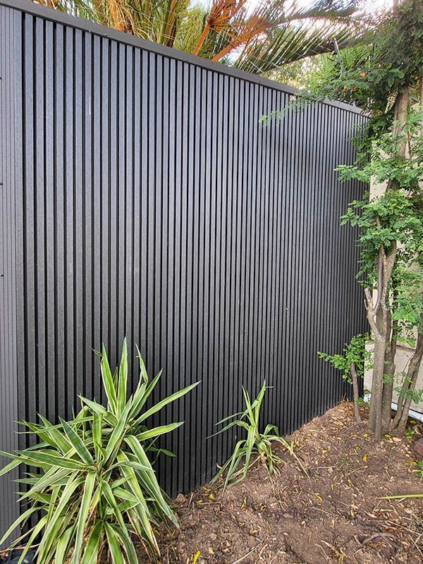 A black fence is surrounded by plants and trees in a garden.