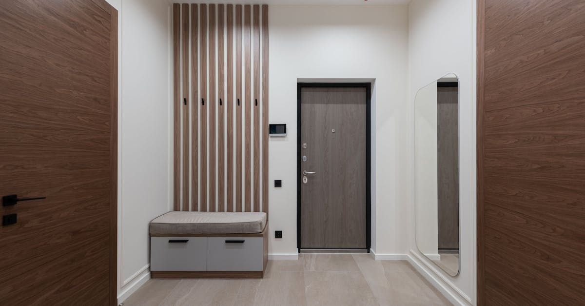 A hallway with a door , a bench , a mirror and a coat rack.
