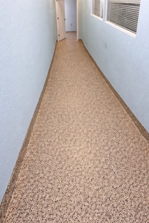 Narrow hallway with speckled flooring, blue walls, and a window. A door is open at the end.