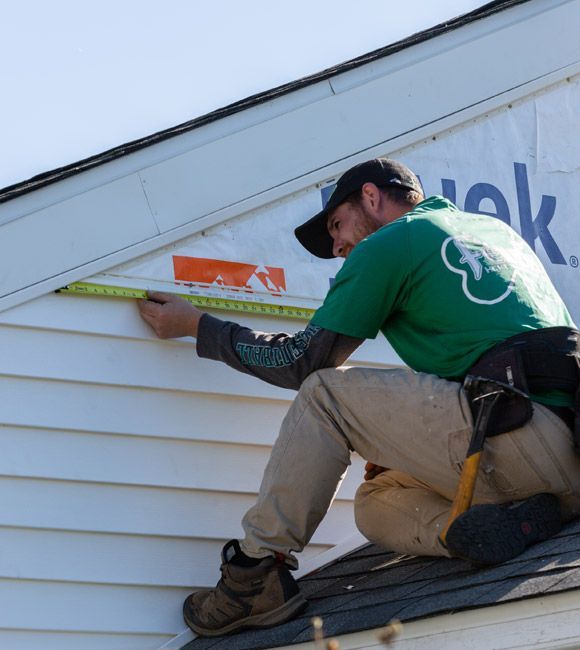 A man in a green shirt is measuring a wall with a tape measure