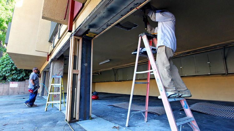 A man on a ladder is working on a garage door.
