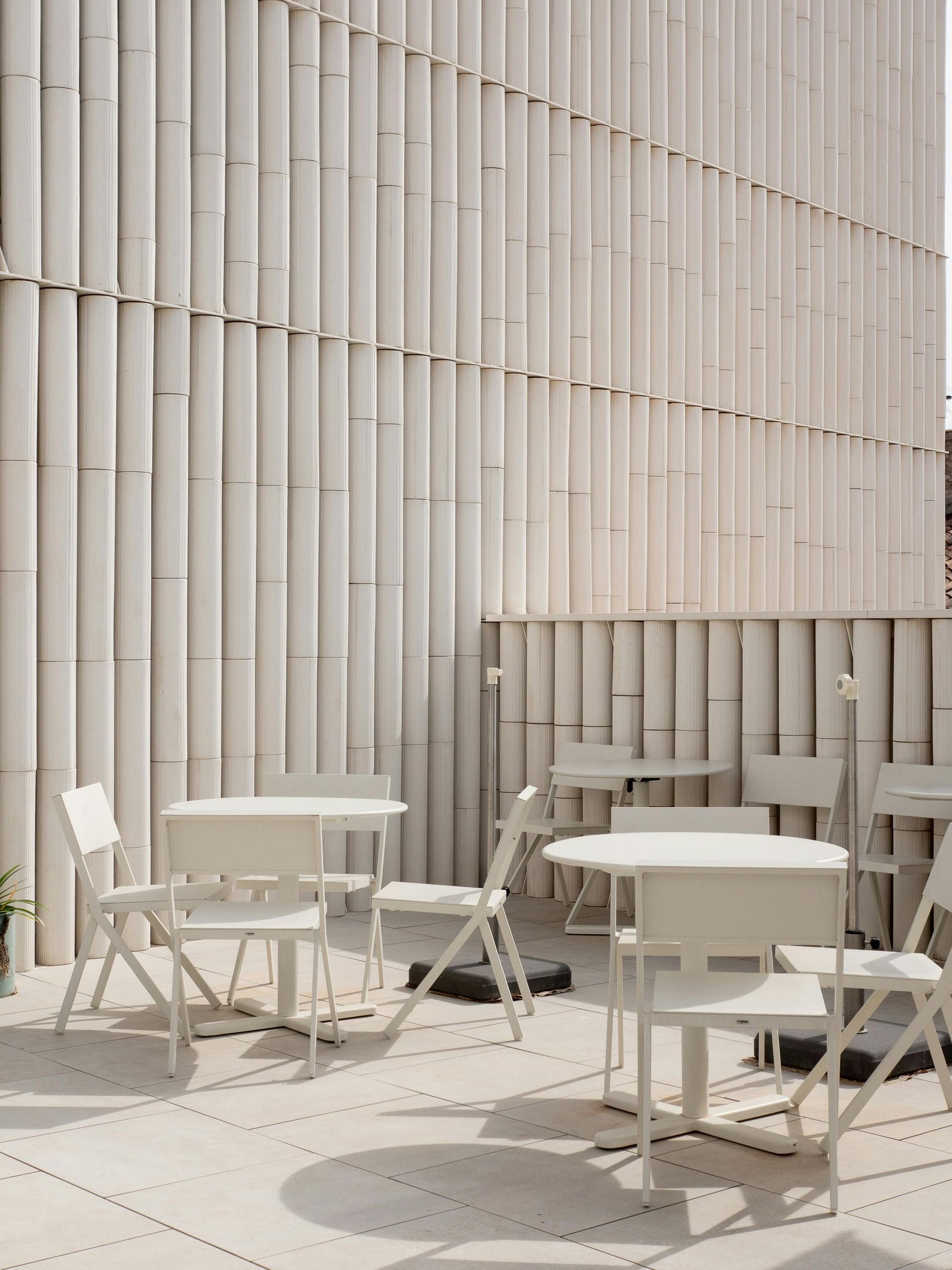 A patio with tables and chairs in front of a white wall.