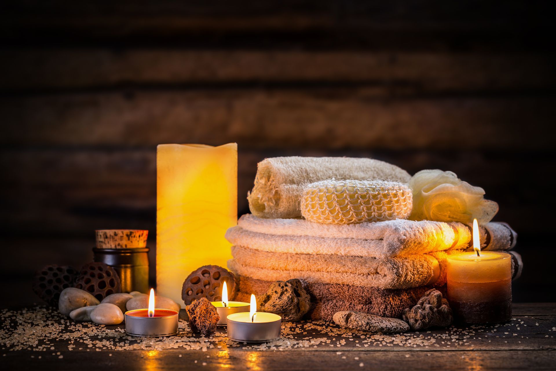 Candles, towels, loofahs, and stones arranged for a spa setting, with warm lighting against a wooden backdrop - Thames, NZ - Thai Classic Massage Thames