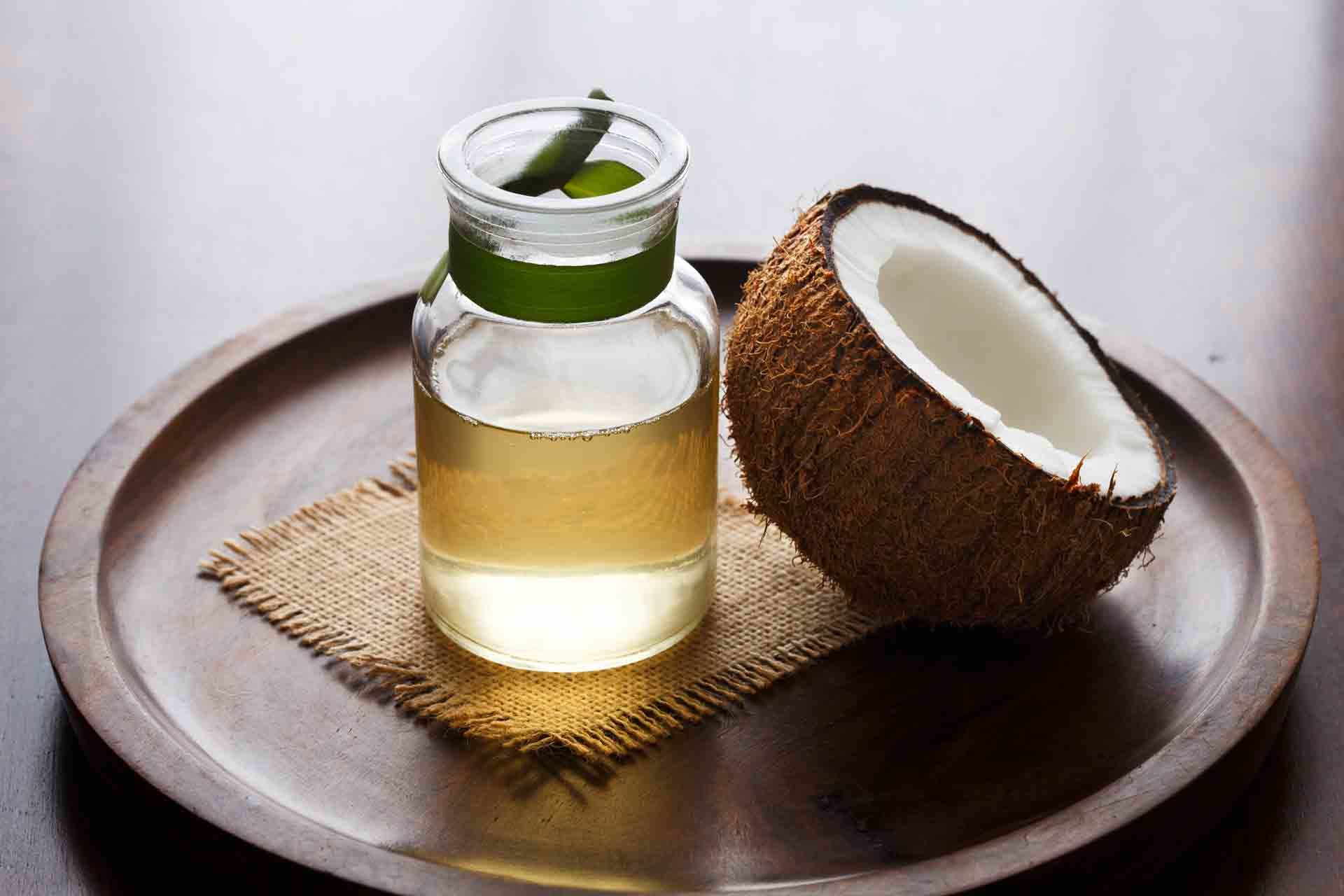 A clear glass bottle of coconut oil and a half-cut coconut sit on a wooden tray - Thames, NZ - Thai Classic Massage Thames
