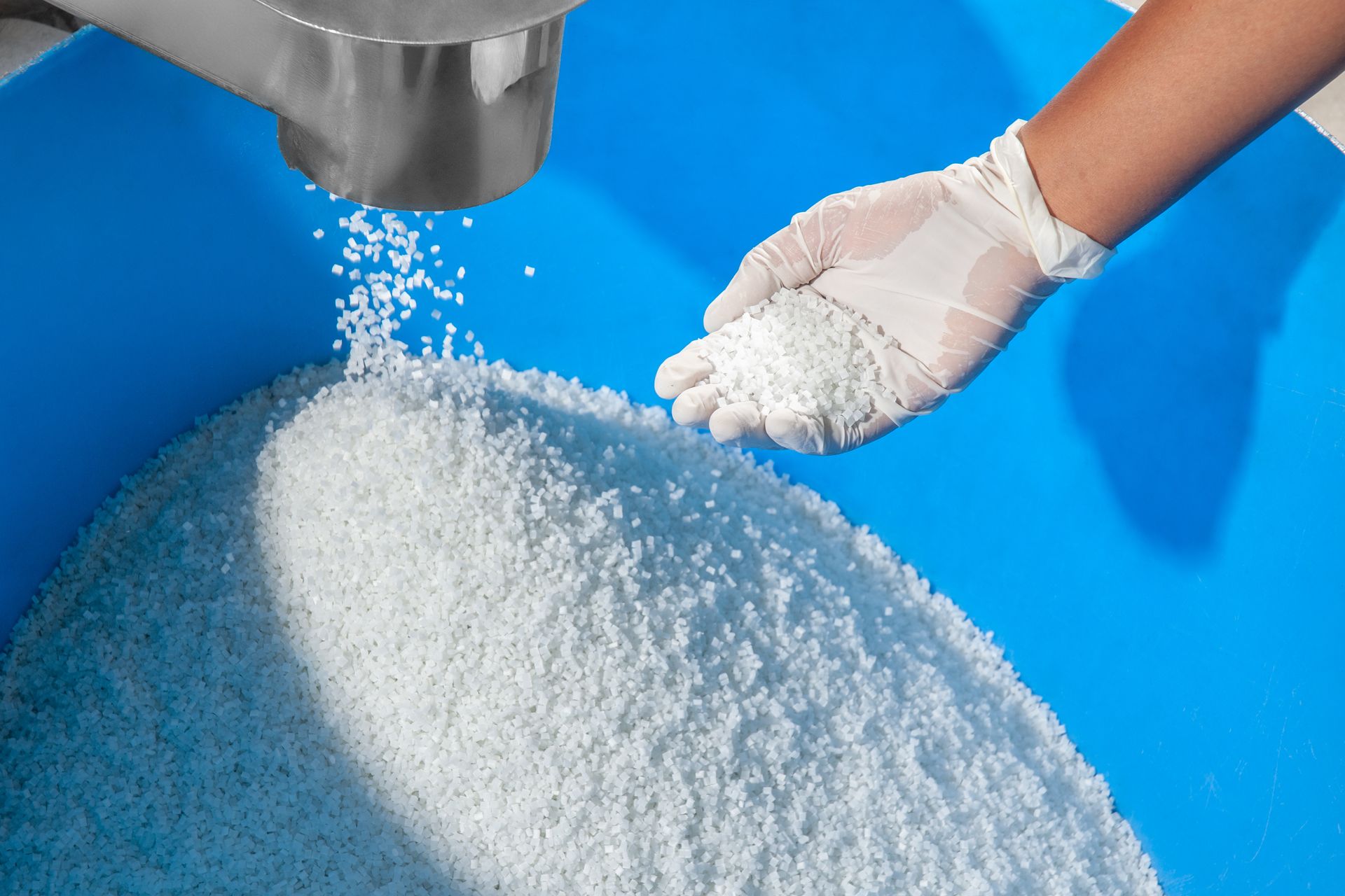 A person wearing white gloves is pouring white powder into a blue container