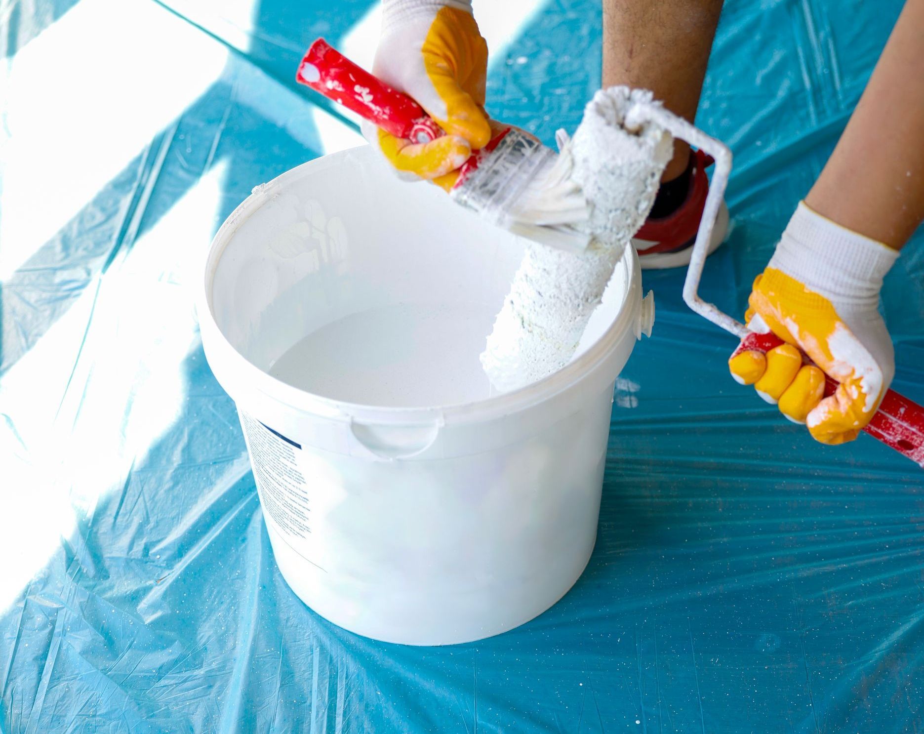 A person is holding a paint roller over a bucket of white paint