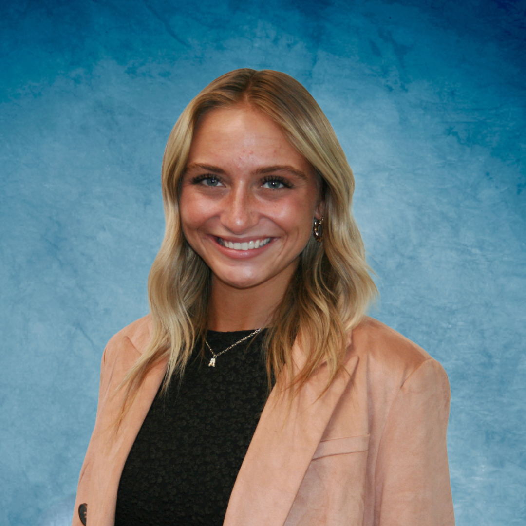 A woman in a white tank top is smiling in front of a blue background.