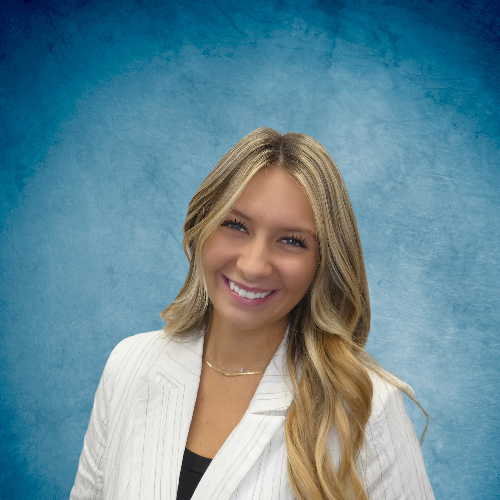 A woman in a white jacket is smiling in front of a blue background.
