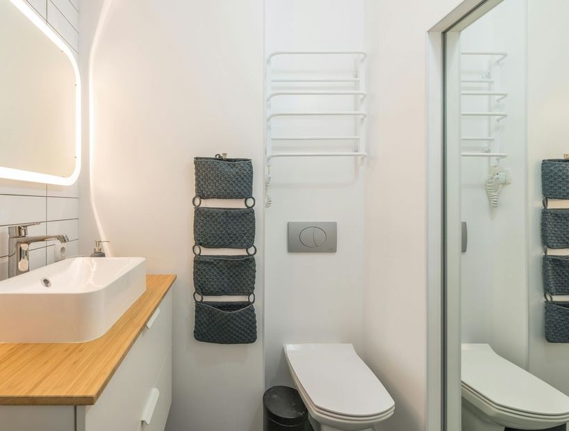 Modern bathroom with white sink, toilet, towel rack, mirror, and woven storage baskets