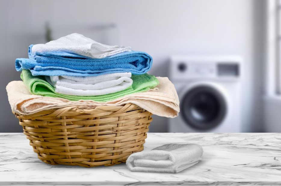 Laundry basket with folded towels on a white table, with a washing machine blurred in the background