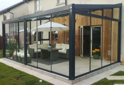 A patio with a couch , table and umbrella in front of a house.