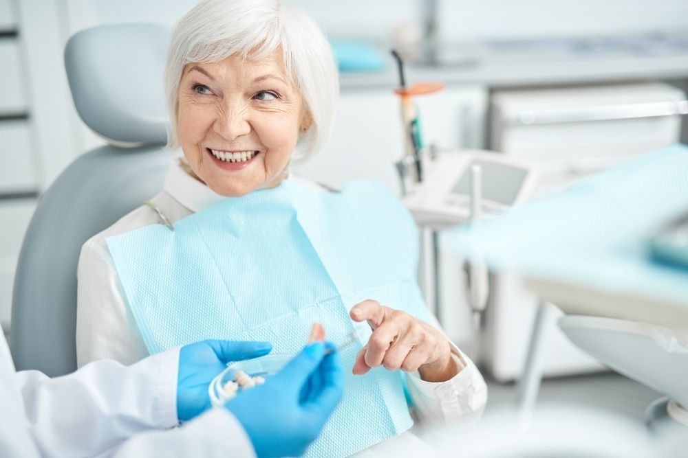 Woman at dentist's office smiles as dentist shows her something. Blue gloves, white coat, and dental chair.
