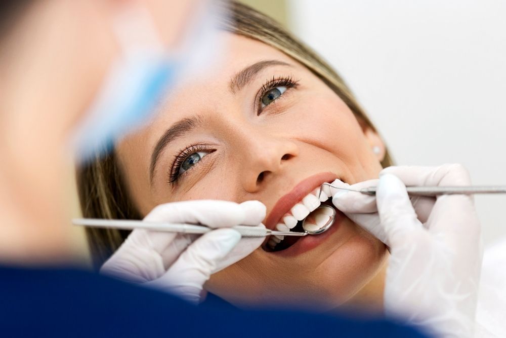 Woman at a dentist's office, smiling as dentist examines her teeth.