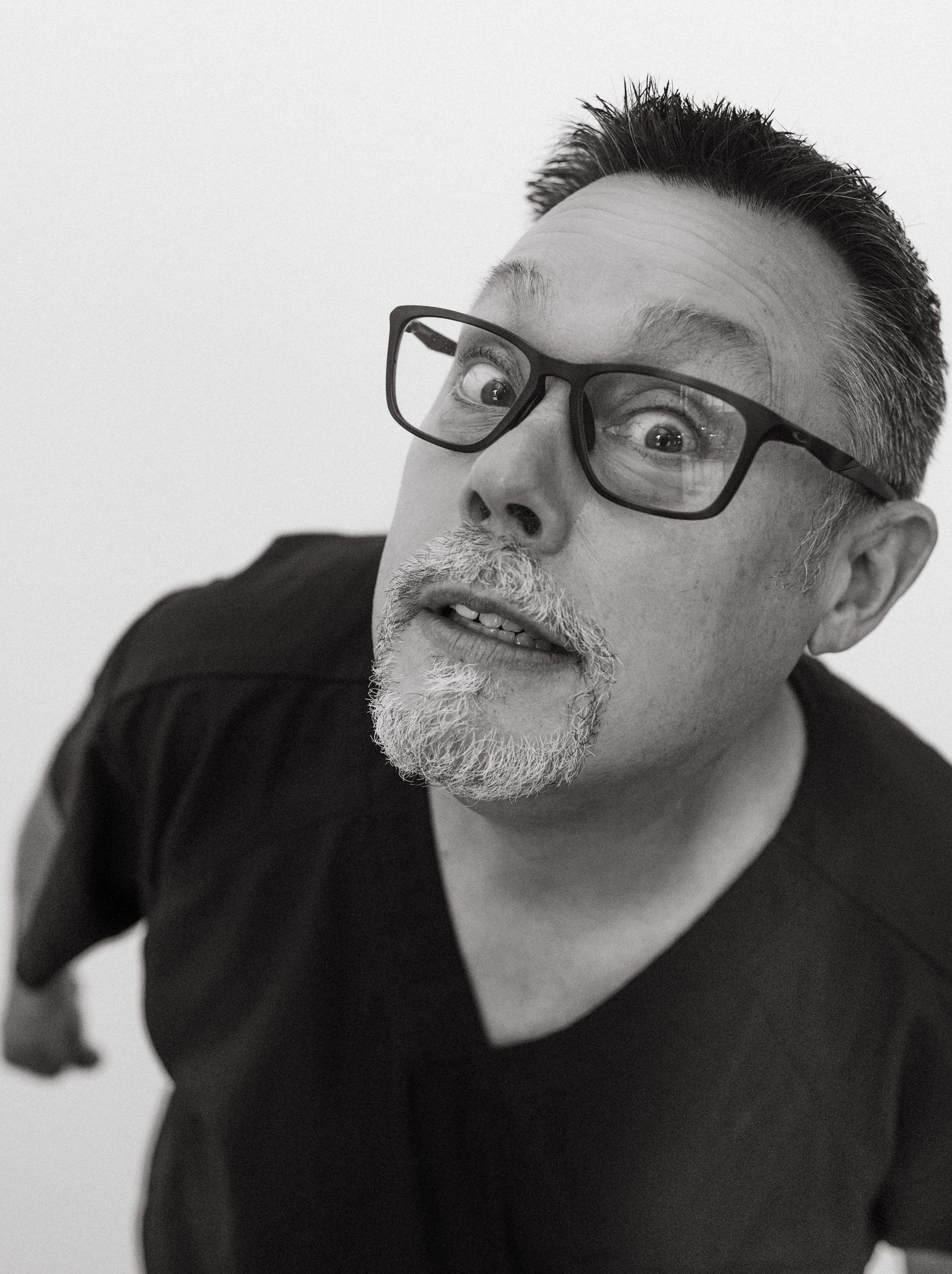 Man with glasses looking upward, surprised expression, in front of a white background.