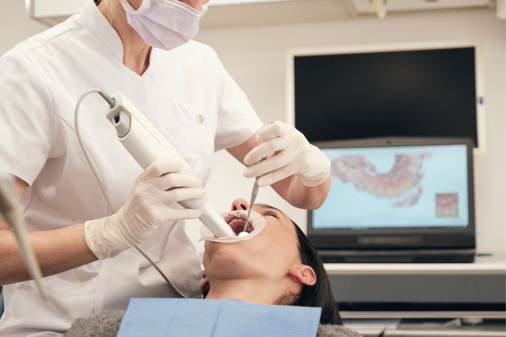 Dentist using a scanner on a patient's teeth in a dental office. Patient is reclined.