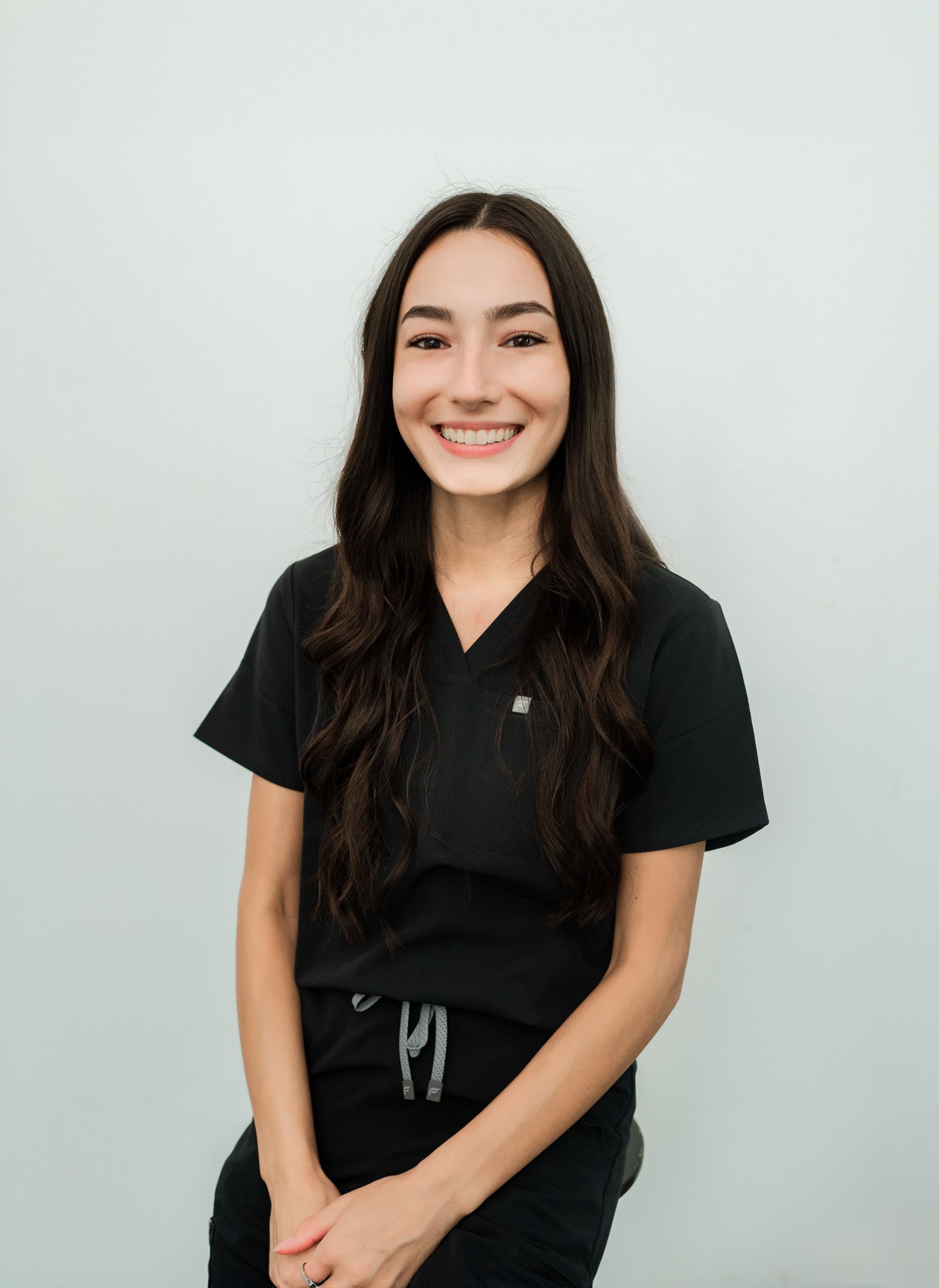 Woman in black scrubs smiles, against a white wall.