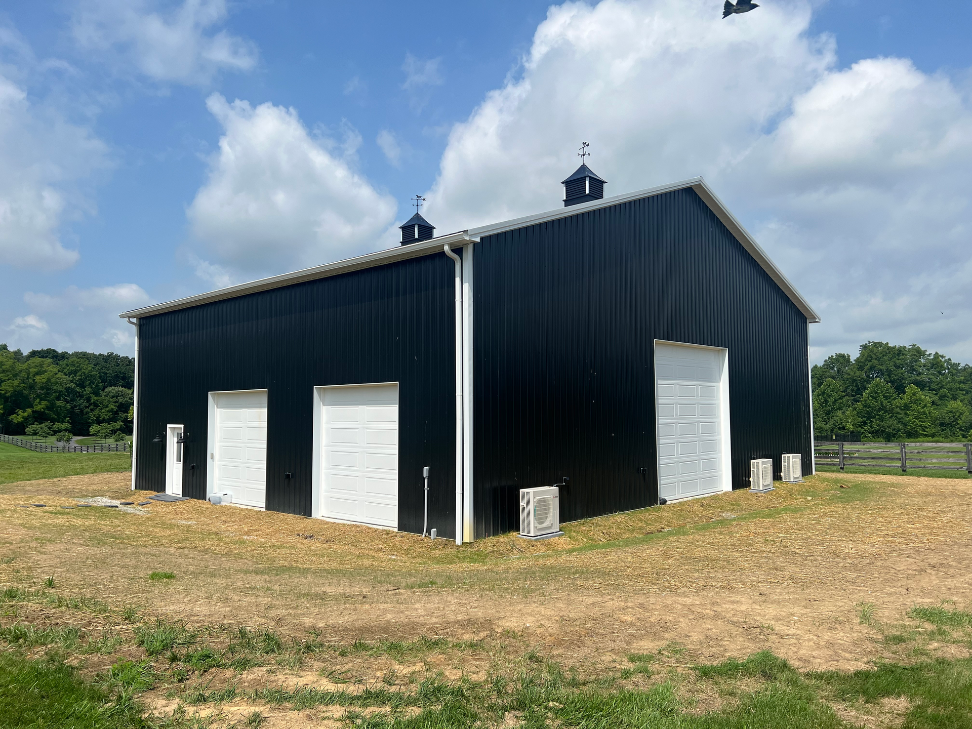 Black metal barn with white doors under a blue sky. The barn sits in a grassy field.