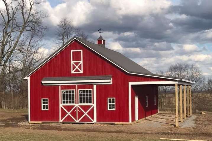 Red barn with white trim and a covered side porch under a cloudy sky.