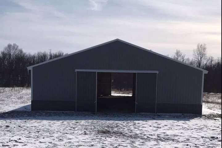 Gray metal barn with open sliding doors on a snowy field under a blue sky.
