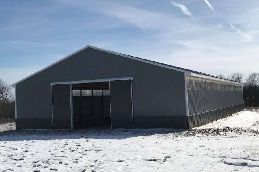A gray metal barn with a large open doorway, set against a snowy landscape and blue sky.