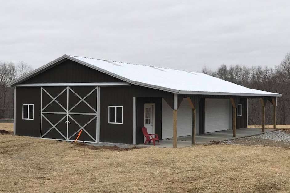 Brown metal barn with white roof, porch, and sliding doors, on a grassy plot under a cloudy sky.