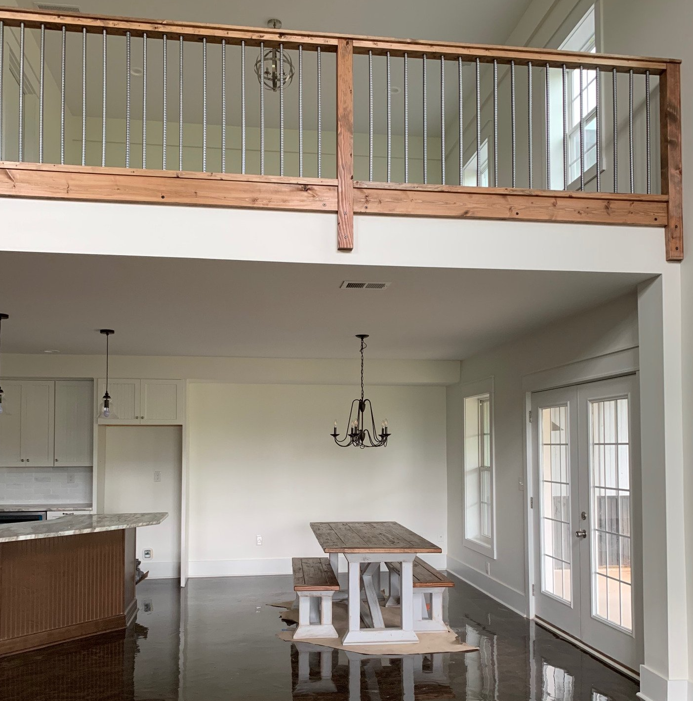 Interior with a loft, kitchen, and dining area.  A wooden balcony overlooks the space with white walls, a kitchen island, and a dining table.