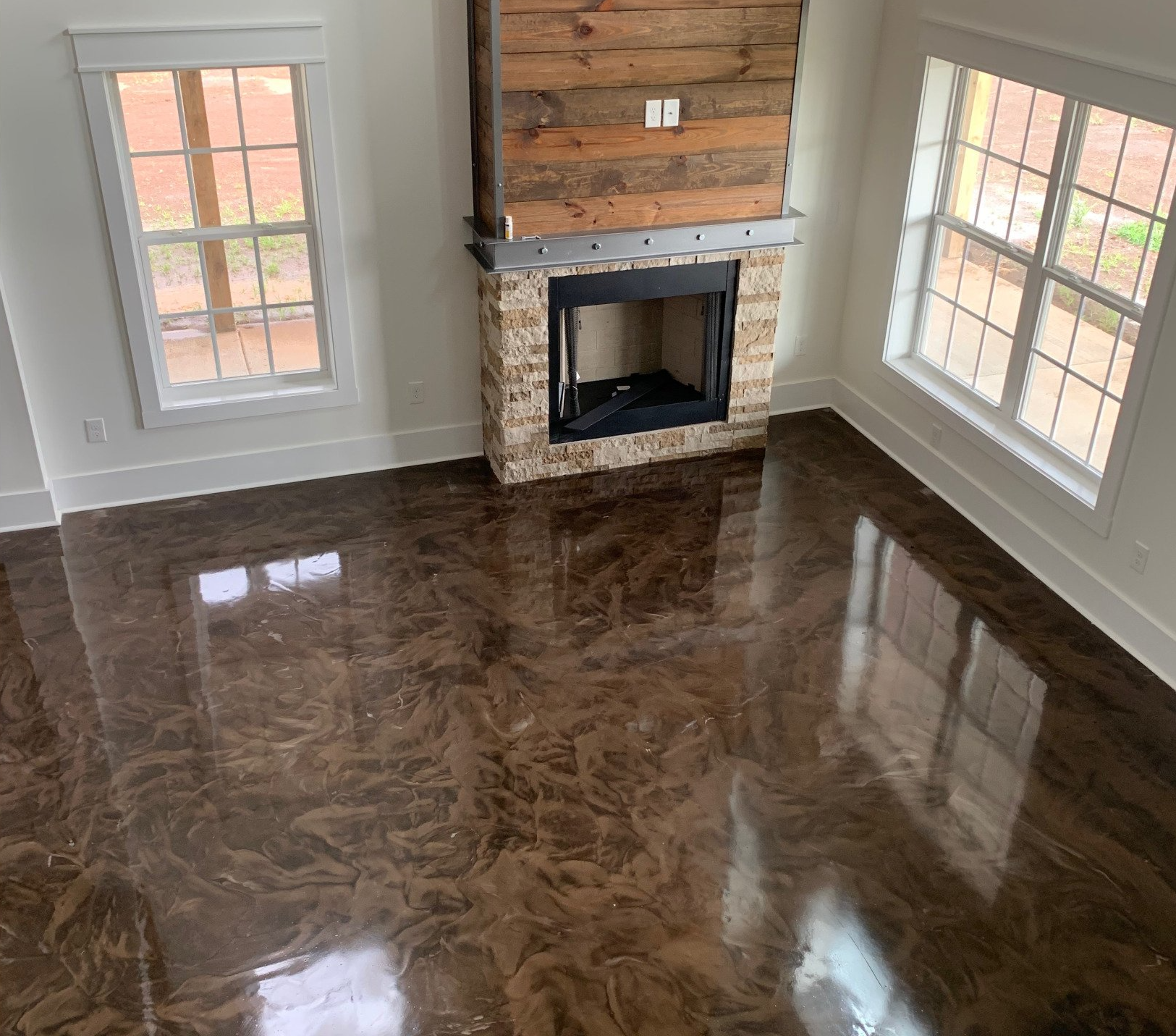 High-angle shot of a living room with a fireplace, two windows, and a glossy, brown epoxy floor.