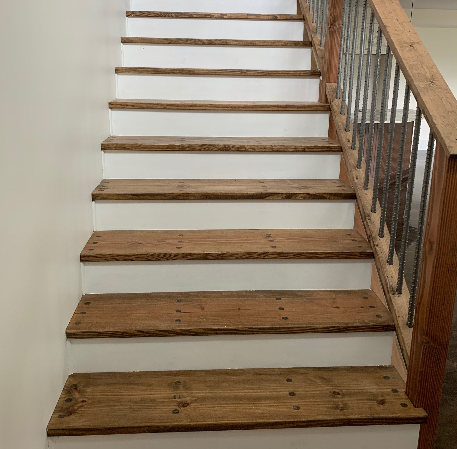 Wooden stairs with white risers and a rustic wooden handrail and metal balusters.