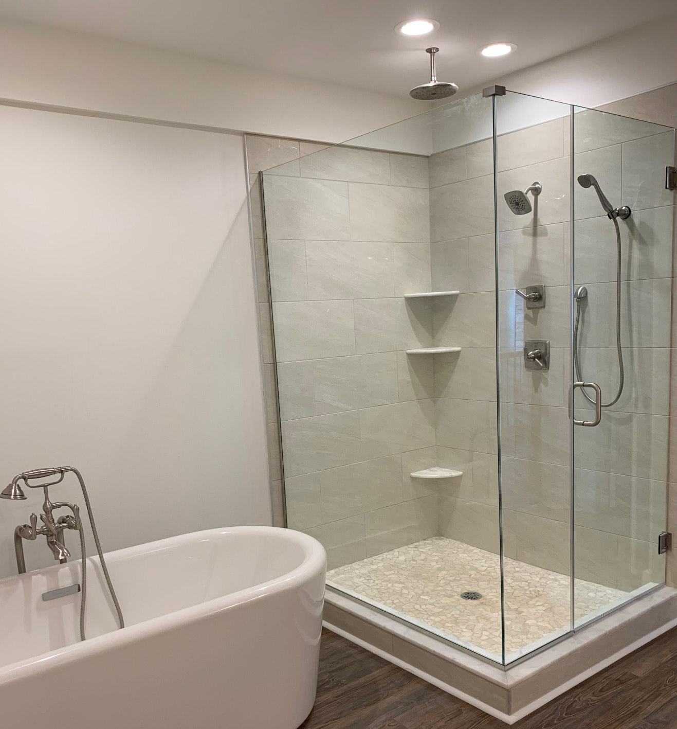 Modern bathroom with a freestanding tub and a glass-enclosed shower featuring a pebble floor, tiled walls, and built-in shelves.