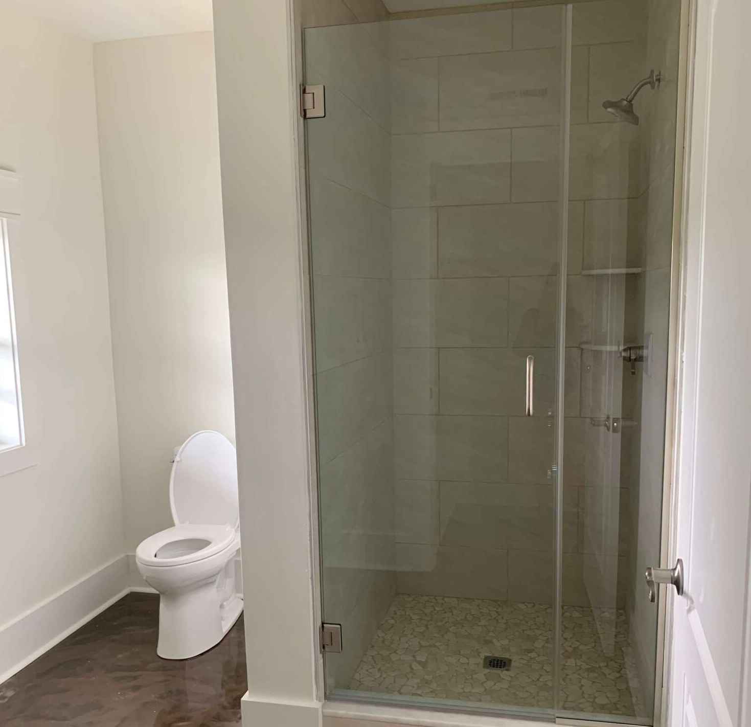 Bathroom with a frameless glass shower, white toilet, and stone tile flooring.  Walls are white.
