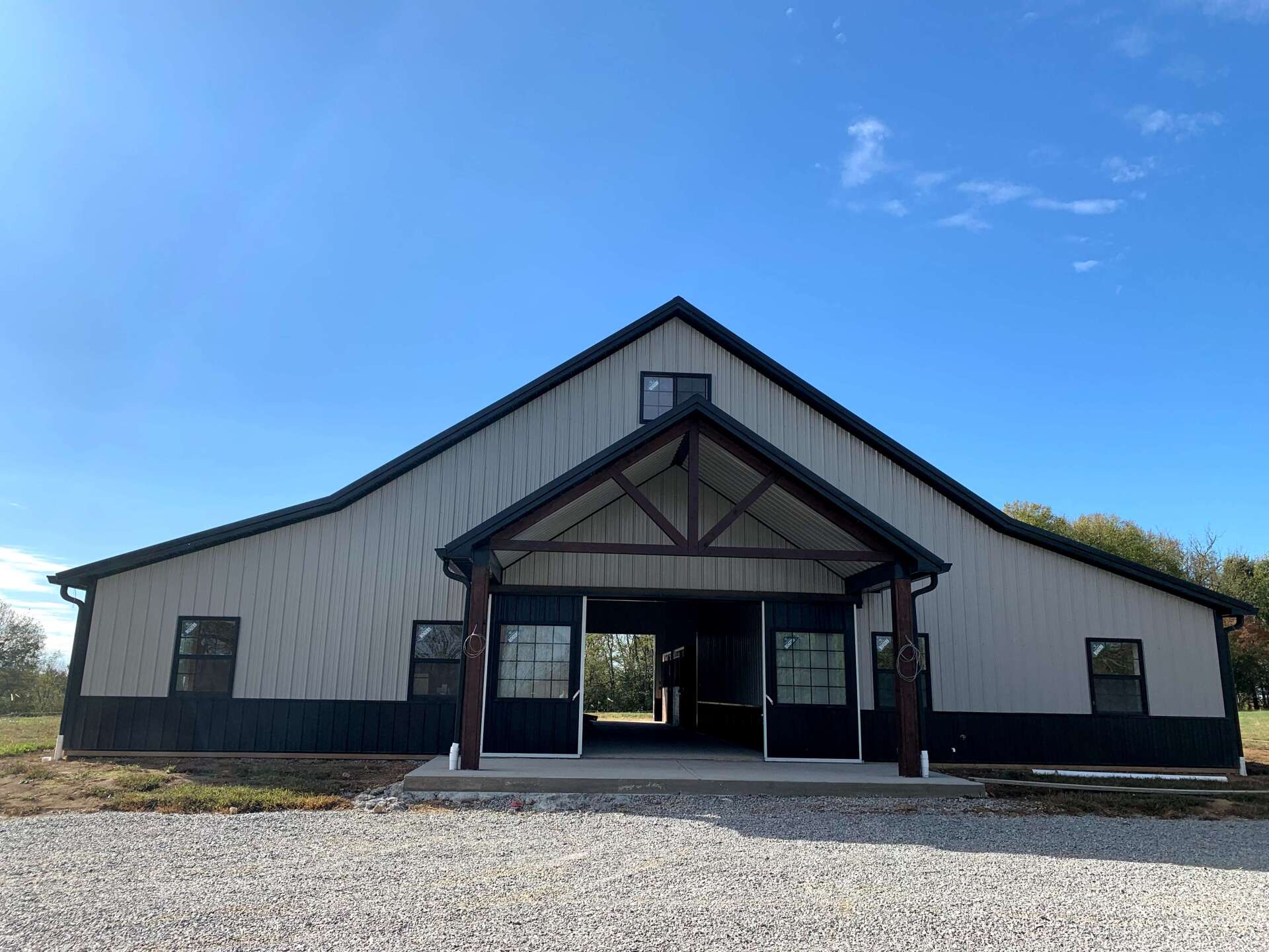 A gray barn-style building with a black roof and trim, and a gravel driveway. The entrance has a brown wood awning.
