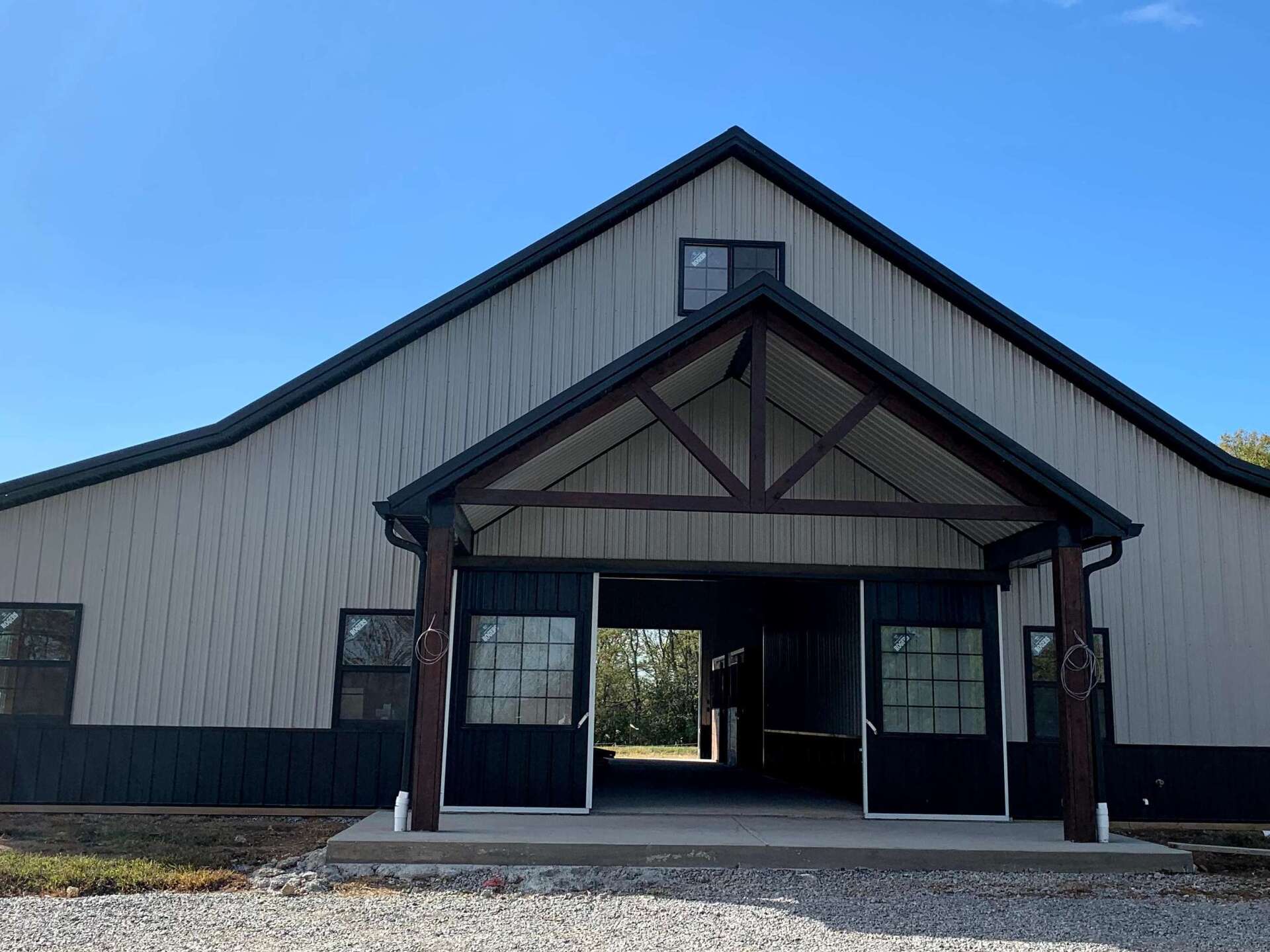 Exterior of a large gray barn with a dark-trimmed entrance. Open doors reveal the interior.