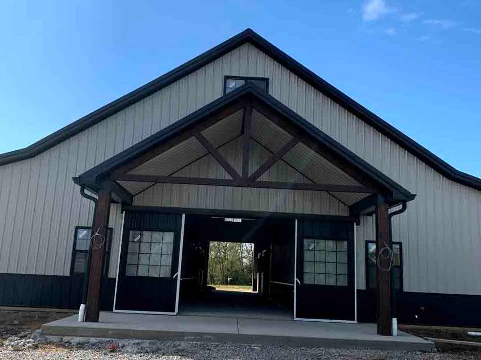 Barn entrance with dark brown trim, open black doors, and a concrete walkway on a sunny day.