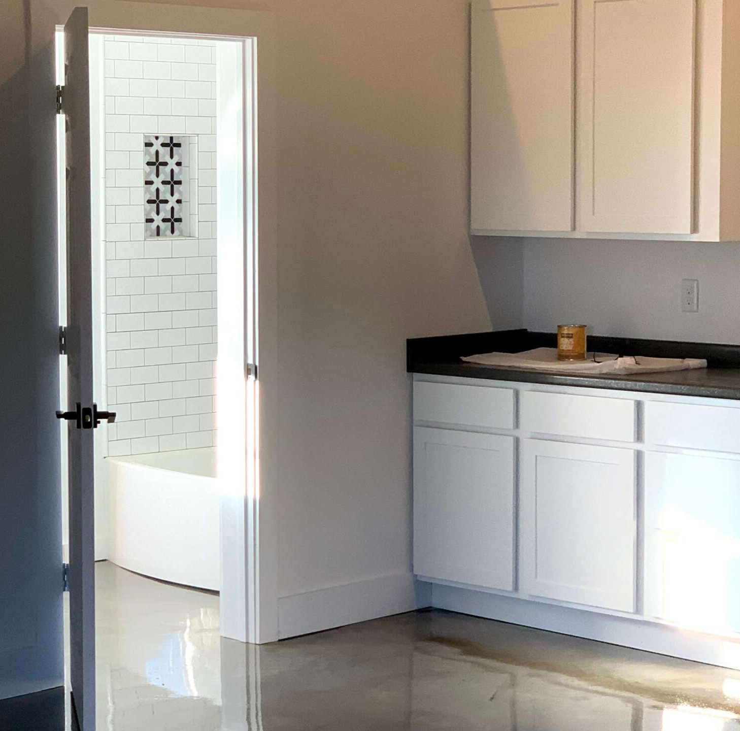 A partially open white door reveals a bathroom with a tiled shower. A cabinet and countertop are visible in the foreground.