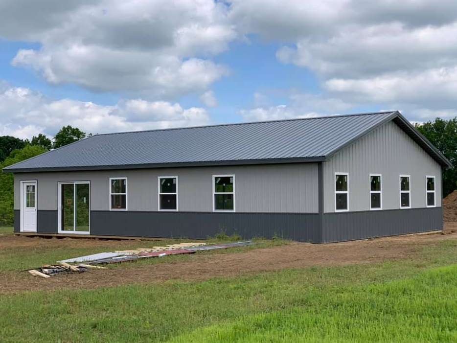 A metal building with gray and dark gray siding and a dark gray roof. White-framed windows and a glass sliding door are visible.