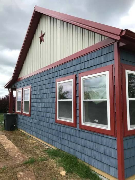 Blue shingled house with red trim and a star on the gable. Three windows on the side.