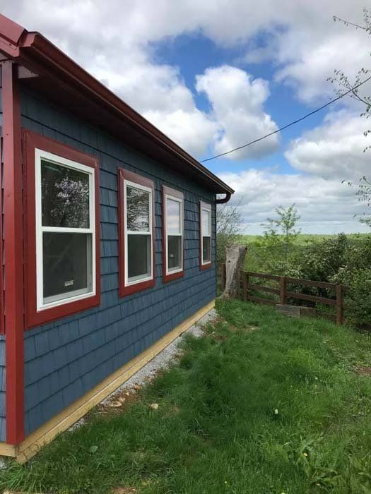 Blue house with red trim and white windows, set on a grassy yard with a view of a cloudy sky.
