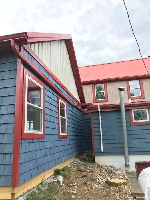 Blue shingled building with red trim and a red roof. A section of the building is tan with a red roof.