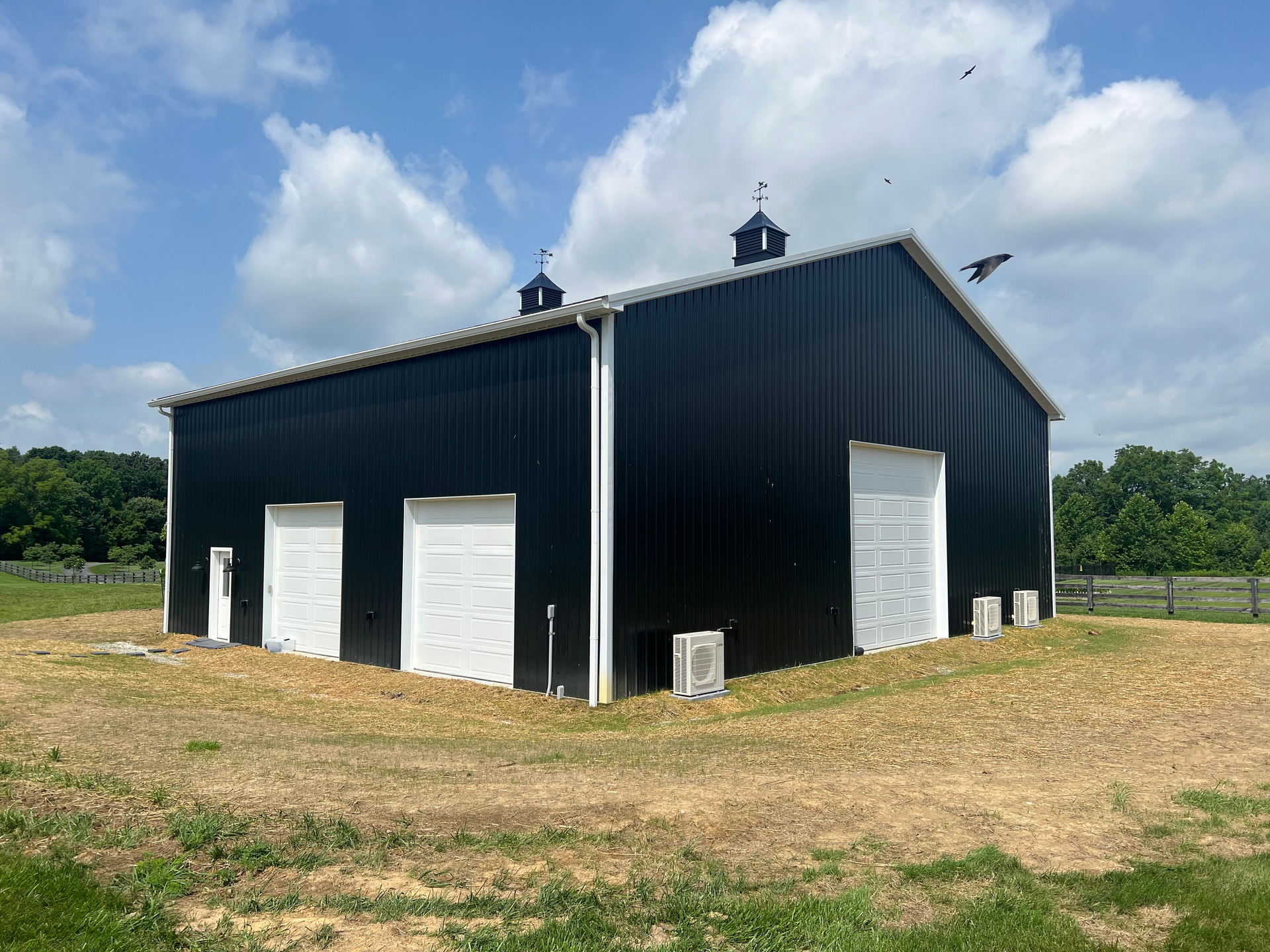 Black metal barn with white doors and trim under a partly cloudy sky.