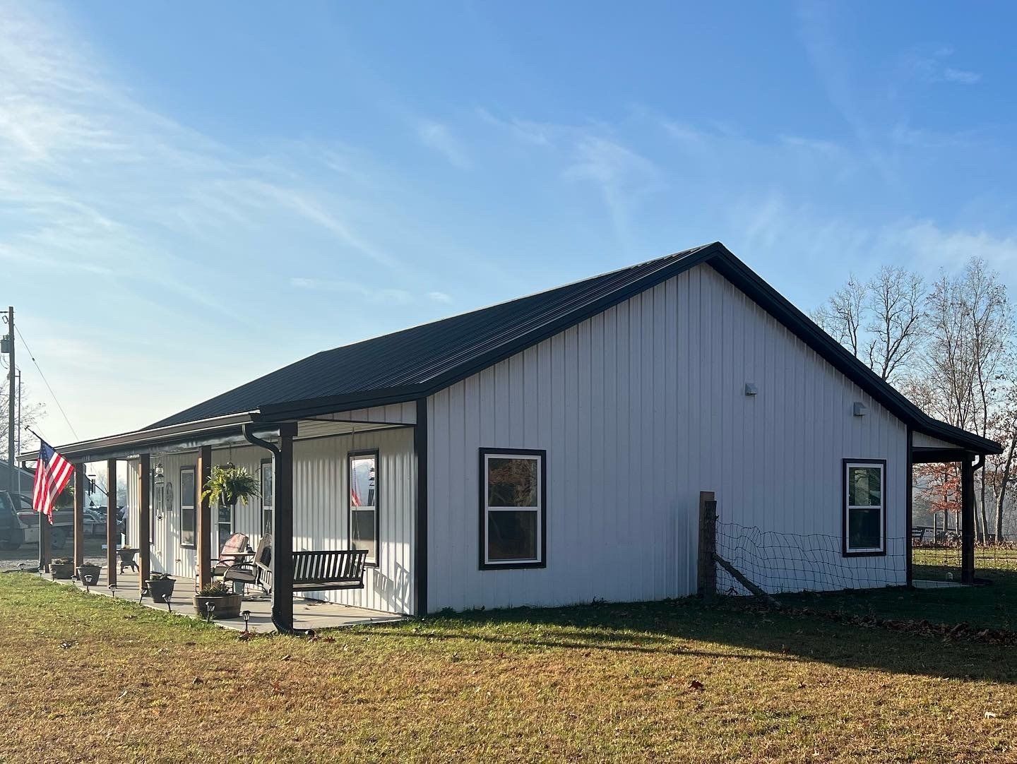 White farmhouse with a black metal roof and a porch. An American flag hangs on the porch.