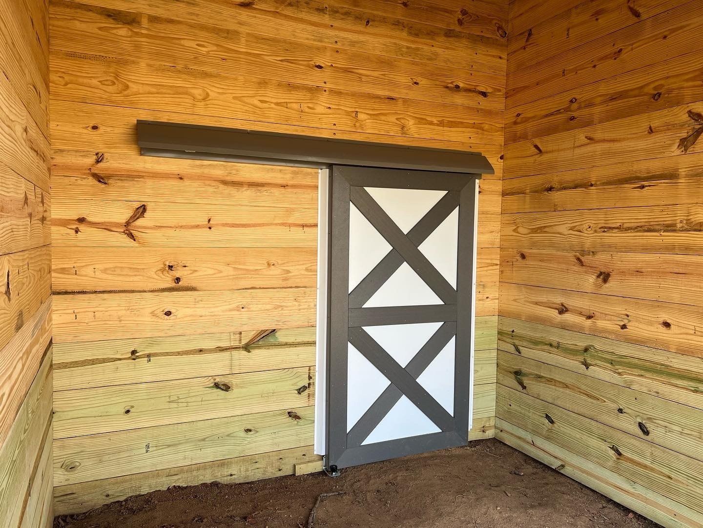 Interior view of a wooden shed with a white and gray barn door. Horizontal wooden planks make up the walls.